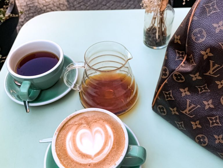 Louis Vuitton Bag Sitting On Table With Cup Of Coffees